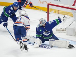 Oilers Adam Erne shoots the puck past Vancouver goalie Thatcher Demko as Canucks defender Ian Cole reaches in with his stick.