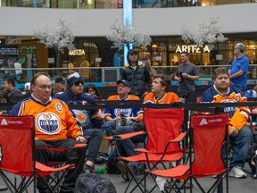 Fans, many in Oilers gear, sit in camp chairs in a roped-off area of the Ice Palace, with mall shops seen in the background