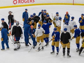 OIlers players and coaches mill around on the ice at Rogers place, with the players wearing beige throwback hockey pants with their practice uniforms