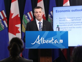 Finance Minister Nate Horner speaks behind a podium with "Alberta" on the front against a backdrop with a projection of economic statistics flanked by Canadian and Alberta flags