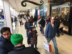 shoppers carrying bags walk past stores with Christmas decorations in West Edmonton Mall