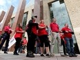 People in red T-shirts holding signs stand outside city hall