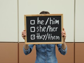 A person holds a chalkboard with list of gender pronouns.