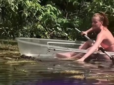 Screenshot of woman in clear kayak petting an alligator in the water.