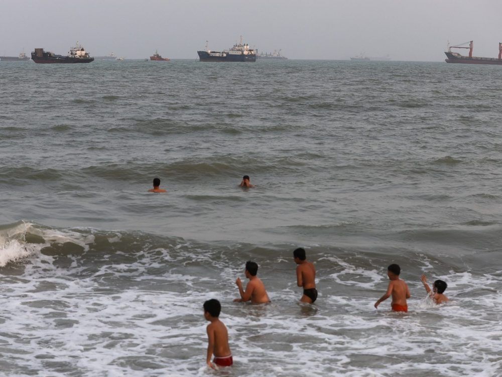 Children swim as ships are seen anchored in the Strait of Hormuz on August 10, 2026 off the coast of Bandar Abbas, Iran.