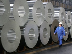 A worker walks among rolls of semi-finished aluminum.