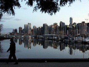 A man walks in Stanley Park as the skyline of Vancouver is reflected in water in Vancouver.