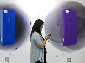 A woman uses her iPhone as she walks past an advertisement featuring iPhone cases at the Macworld iWorld expo in Beijing, China, Thursday, Aug. 22, 2013
