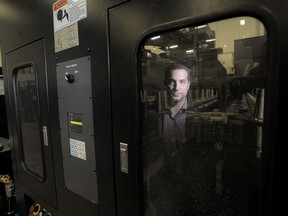 Alexander Cajic, vice-president, business development at Koss Aerospace, is reflected in the window of a flexible robot cutting machine that can shift from part to part without downtime.