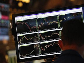 A screen displays stock charts while a trader works at his post on the floor at the New York Stock Exchange