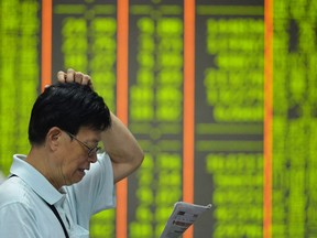 An investor reads a newspaper before a screen showing share prices at a securities firm in Hangzhou, in eastern China's Zhejiang province