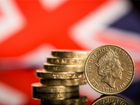 A stack of British one pound sterling coins stand in front of a British Union flag.