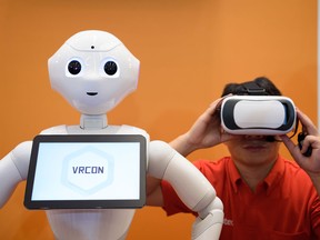 An attendee uses a Google Inc. Cardboard virtual reality headset beside SoftBank Group Corp.'s Pepper the humanoid robot during a press preview ahead of the Pepper World 2016 Summer event in Tokyo, Japan, on Wednesday, July 20, 2016.