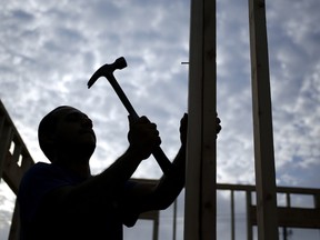 The silhouette of a contractor is seen hammering wood framing for a house under construction