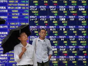 A man looks up at the sky in front of an electronic stock indicator of a securities firm in Tokyo, Thursday, Aug. 18, 2016.