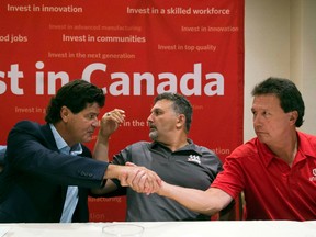 Unifor national president Jerry Dias, left, shakes hands with bargaining committee member Chris Taylor, right, of Ford Motor Company, as bargaining committee member Dino Chiodo, of Fiat Chrysler, sits between them.