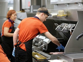 An employee cooks hamburger patties in the kitchen of a fast food restaurant.