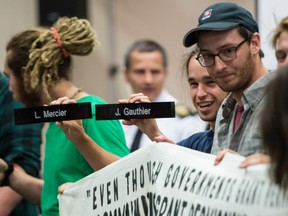 A demonstrator holds up the name plates of two of the commissioners as they disrupt the National Energy Board public hearing into the proposed $15.7-billion Energy East pipeline project