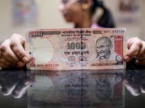 An Indian bank employee displays a one-thousand rupee note.