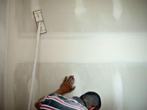 A man uncovers a wall outlet as he finishes drywall in a new home under construction