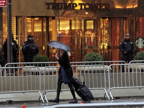 A woman under an umbrella pulls her suitcase on Fifth Avenue by police barricades outside the Trump Tower building in New York, Tuesday, Nov. 15, 2016. Sequestered in his Manhattan high-rise, President-elect Donald Trump is preparing to fill key foreign policy posts.