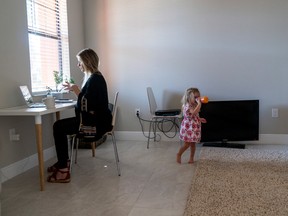 Erin Fahs uses her computer for a conference call for her job, while her daughter Amelia, 2, plays at their home in Fort Myers, Fla.