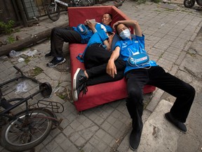 Food delivery drivers rest on an abandoned couch on a sidewalk in Beijing. The Moody's ratings agency on Wednesday cut China's credit rating due to surging debt, prompting a protest by Beijing and highlighting challenges faced by communist leaders as they overhaul a slowing economy.