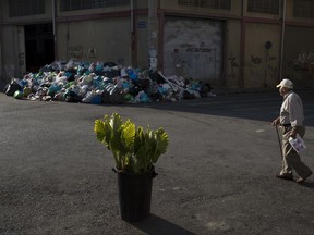 A man looks on a pile of trash as he walks behind a flower pot in Kaminia neighborhood of Piraeus, near Athens Tuesday,  June 27, 2017. Striking garbage collectors are on the 11-day of protest that left huge piles of trash around Athens. (AP Photo/Petros Giannakouris)