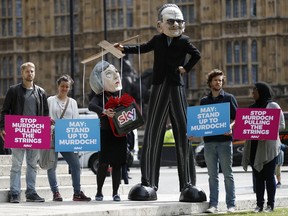 Campaigners from the community-based organization Avaaz, wearing a mask of Rupert Murdoch, centre right, and Prime Minister Theresa May, stage a protest opposite parliament in London, Thursday, June 29, 2017. Britain's Culture Secretary Karen Bradley  is ruling on whether to permit the proposed 11.7 billion pound merge of Sky and Twenty-First Century Fox.  Bradley is set to offer her verdict Thursday. The merger would allow Rupert Murdoch to consolidate his power base in British media. (AP Photo/Frank Augstein)
