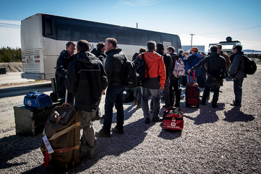Workers line up to take the bus to the airstrip, where they’ll fly home for two weeks.