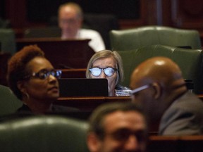 FILE - In this June 28, 2017, file photo, Rep. Barbara Flynn Currie, D-Chicago, center, works on a laptop at her desk on the House floor at the Capitol in Springfield, Ill. Illinois is hours away from entering its third fiscal year without a state budget, territory that could mean some universities won't be able to offer federal financial aid, road construction and Powerball ticket sales will halt and the state's credit rating will be downgraded to "junk." (Rich Saal/The State Journal-Register via AP File)