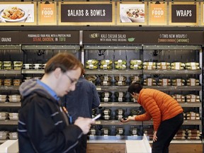 FILE - In this Thursday, April 27, 2017, file photo, shoppers roam through an Amazon Go store, currently open only to Amazon employees, in Seattle. Amazon Go shops are convenience stores that don't use cashiers or checkout lines, but use a tracking system that of sensors, algorithms, and cameras to determine what a customer has bought. Amazon's nearly $14 billion deal for Whole Foods isn't just about getting more than 460 grocery stores. Ultimately, Amazon wants to sell Amazon and Whole Foods shoppers alike even more goods and services, including stuff they might not even realize they need. (AP Photo/Elaine Thompson, File)