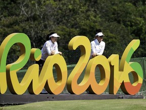 FILE - In this Aug. 16, 2016 file photo, Kelly Tan, left, and Michelle Koh, both of Malaysia, pose for a photo with the Rio 2016 logo on the 16th hole during a practice round for the women's golf event at the 2016 Summer Olympics in Rio de Janeiro, Brazil. Almost a year after the Rio Olympics, Brazilian organizers are asking for help from the International Olympic Committee in order to pay creditors. (AP Photo/Chris Carlson, File)
