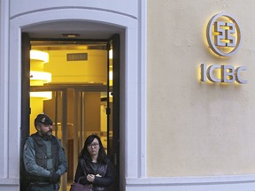 In this Wednesday, Feb. 17, 2016, file photo, a woman walks past a Spanish Civil Guard policeman as she leaves an Industrial and Commercial Bank of China, or ICBC, branch in Madrid, Spain.