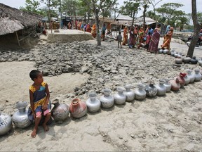 FILE - In this photo taken Friday, May 14, 2010, a village girl sits on a vessel as she waits with others in a queue for water supplied by tankers at an area affected by last year's cyclone Aila in Nildumur, Satkhira district, about 176 kilometers (110 miles) southwest of the capital Dhaka, Bangladesh. A report by the Asia Development Bank on Friday, July 14, 2017, says Asia will endure extreme heat, rising sea levels, growing losses from severe weather and increasing food insecurity in coming decades as climate change raises temperatures and alters weather patterns across the globe. Up to a quarter of Bangladesh is inundated in a normal year, and century-level flooding could put 60 percent of the country under water, the report says. Storm surges from tropical cyclones, destructive winds and landslides are other risks from weather extremes. (AP Photo/Pavel Rahman, File)