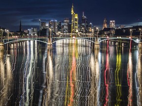 In this photo taken Sunday, July 30, 2017, the skyline of the city is reflected in the river Main during night time behind the Ignatz-Bubis bridge in Frankfurt, central Germany. The picture was taken with long time exposure and a vertical movement of the camera. (Frank Rumpenhorst/dpa via AP)