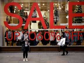FILE - In this file photo dated Friday, Dec. 23, 2016, people pass a sale sign in a shop window off Oxford Street in London. According to official figures released by Office for National Statistics Wednesday July 12, 2017, household incomes in Britain are being squeezed even though unemployment has fallen to its lowest level since the mid-1970s, amidst uncertainty as the country's exit from the European Union looms nearer. (AP Photo/Matt Dunham, FILE)