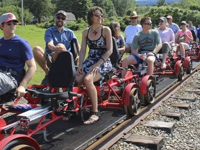 In this July 8, 2017 photo, a Rail Explorers tour stops to admire the view by the Mount Hope Bridge in Portsmouth, R.I. Rail Explorers opened in Portsmouth in April as part of the Newport and Narragansett Bay Railroad. Visitors can ride a rail bike and travel six miles along tracks that were once part of the Old Colony Railroad. (AP Photo/Jennifer McDermott).