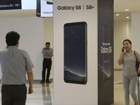 People use their smartphones near an advertisement of the Samsung Electronics Galaxy S8 smartphone at its shop in Seoul, South Korea