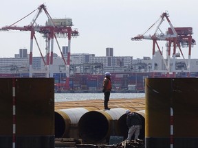 FILE- In this March 24, 2017, file photo, a worker stands at a seaside construction site with the pier of a container terminal in the background in Tokyo.  Japan's exports rose nearly 10 percent in June from a year earlier, while imports jumped 15.5 percent, biting into its trade surplus. A recovery in exports to China and the rest of Asia is helping sustain growth of the world's third-largest economy. The customs figures reported Thursday, July 20, 2017,  showed exports to China surged 20 percent from a year earlier, to 1.25 trillion yen ($11 billion). (AP Photo/Eugene Hoshiko, File)