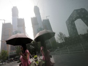 A woman carries an umbrella past a shopping mall's window with reflection of construction buildings at the Central Business District in Beijing, Monday, July 17, 2017. China's economic growth held steady in the latest quarter, boosted by trade and consumer spending, despite concerns about a possible impending slowdown. (AP Photo/Andy Wong)