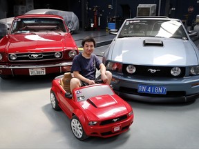In this Wednesday, June 28, 2017, photo, Guo Xin sits on a toy Mustang as he poses with his 1966 MT GT Fastback, left, and 2005 GT convertible at his garage in Beijing. Guo operates a garage in Beijing that repairs and refits Mustangs. He founded a club in 2011 for Mustang admirers that has more than 3,000 members across China. (AP Photo/Andy Wong)