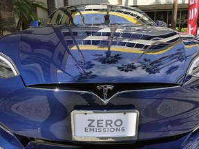 FILE - In this Oct. 24, 2016, file photo, palm trees are reflected on the hood of a Tesla Model S on display in downtown Los Angeles. California could spend up to $3 billion under a bill that would widely expand its consumer rebate program for zero-emission vehicles. The Legislature is pushing forward a bill that could lift rebates from $2,500 to $10,000 or more for a compact electric car. Current rebates have done little to boost sales. (AP Photo/Richard Vogel, File)