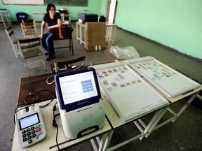 FILE - In this Dec. 6, 2013, file photo, a member of the Venezuelan National Electoral Council waits for a voting machine to charge during the preparation of a polling station in Caracas, Venezuela. Digital voting machines are in the spotlight in Venezuela, where a maker of election systems used in the country's tumultuous constituent-assembly election said Wednesday that the turnout figure had been "tampered with." That meant it was off by at least 1 million votes - possibly in either direction. (AP Photo/Fernando Llano, File)