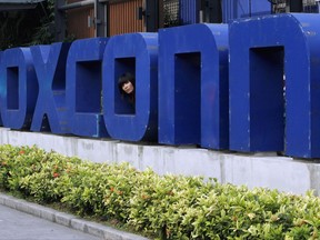 FILE - In this May 27, 2010 file photo, a worker looks out through the logo at the entrance of the Foxconn complex in the southern Chinese city of Shenzhen. The Wisconsin Assembly plans to approve a $3 billion tax break bill for Taiwan-based Foxconn Technology Group to build a new display panel factory in the state. The incentive package up for a vote Thursday, Aug. 16, 2017, would be the largest in state history and the biggest to a foreign company in U.S. history. (AP Photo/Kin Cheung, File)