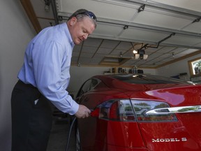 In this Thursday, July 13, 2017, photo, Jeff Solie plugs in his electric Tesla sedan at his home, in New Berlin, Wis. Electric cars are seeing growing support around the world.  But there's a problem: There aren't enough places to plug those cars in.  The nearest fast-charging Tesla Superchargers are 45 miles (72 kilometers) away. There are some public charging stations in nearby Milwaukee, at hotels and shopping centers, but Solie relies almost entirely on the charging system he set up in his garage. (AP Photo/Morry Gash)