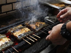In this Aug. 2, 2017 photo, Shinji Hashimoto, sixth-generation owner of a Michelin one-star unagi restaurant in Tokyo, grills Japanese eel that has been coated in a salty-sweet soy sauce marinade, over hot charcoal. Japanese people celebrate the Day of the Ox by indulging in this eel delicacy known as "kabayaki." The endangered Japanese summer delicacy may get a new lease on life with commercial farming. (AP Photo/Sherry Zheng)