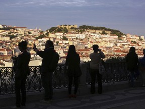 FILE - In this May 25, 2016 file photo, tourists taking pictures are silhouetted against Lisbon's old center lit by the setting sun. Portugal's stock market is surging and its government borrowing rates are falling after the country recovered its investment-grade rating from Standard & Poor's. The Lisbon stock exchange rose more than 1 percent Monday, Sept. 18, 2017 and the 10-year bond yield dropped 0.29 percentage points -- an unusually large one-day increase -- to 2.49 percent, the lowest rate since late 2015. (AP Photo/Armando Franca, File)