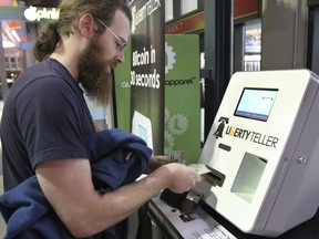 FILE - In this Monday, March 31, 2014, file photo, Tim McCormack, of Boston, inserts cash into a Liberty Teller ATM while purchasing bitcoins at South Station train station, in Boston. On Thursday, Sept. 14, 2017, Bitcoin tumbled 15 percent to about $3,300 against the dollar. (AP Photo/Steven Senne, File)