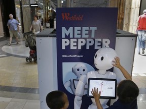 In this Monday, June 26, 2017, photo, James Mak, left, and Marco Mak touch Pepper the robot at Westfield Valley Fair shopping center in San Jose, Calif. Pepper greets shoppers and has the potential to send messages geared to people's age and gender through facial recognition. A San Francisco supervisor is calling for a tax on robots that automate jobs and put people out of work, saying the money should be used to help the unemployed. (AP Photo/Ben Margot)
